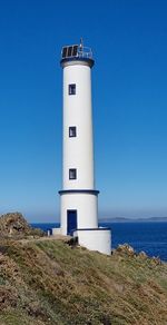 Lighthouse by sea against clear blue sky