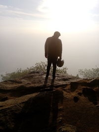 Rear view of man standing on rock against sky during sunrise