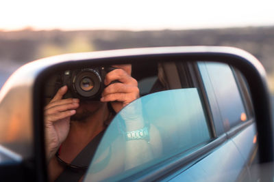 Reflection of man photographing from camera in car