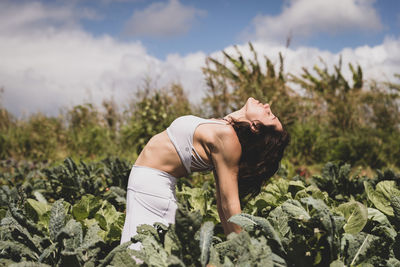Female yogi backbends in field of vegetables