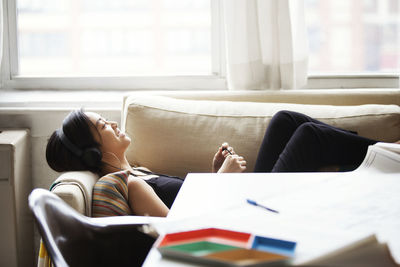 Side view of happy woman listening music while lying on sofa at home