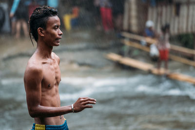 Side view of shirtless man standing on field during rain