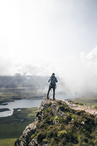 Rear view of young man standing on mountain against sky