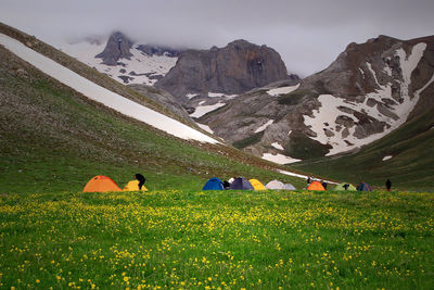 People amidst tents on field against mountains