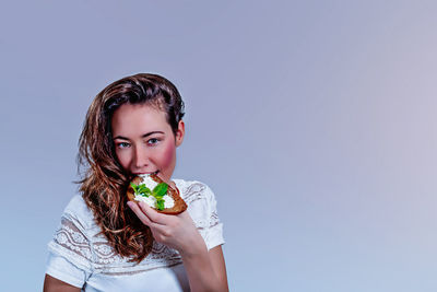 Portrait of beautiful woman eating food against gray background