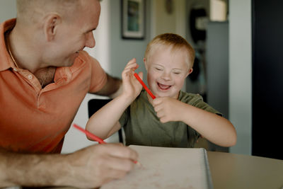 Happy father and son with down syndrome drawing in book at dining table