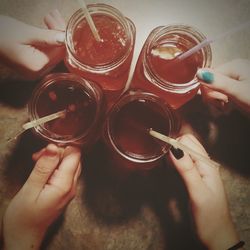 Cropped hands of female friends holding mason jars on table