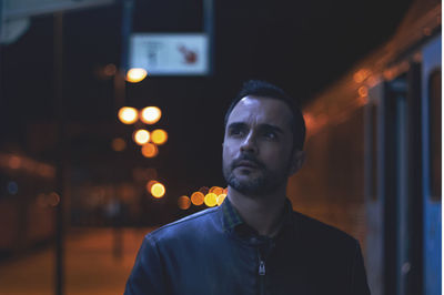 Man looking away while standing at railroad station platform at night