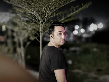 Portrait of young man looking away while standing at night