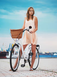 Young woman with bicycle standing on shore against sky