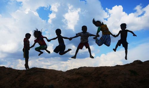 Low angle view of man jumping against cloudy sky