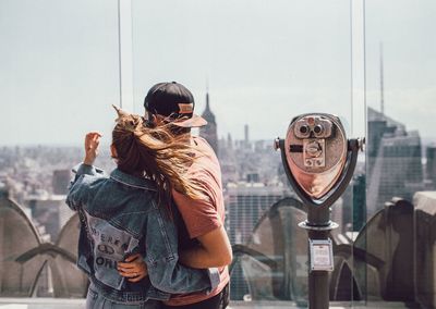 Rear view of couple looking at cityscape by coin-operated binoculars