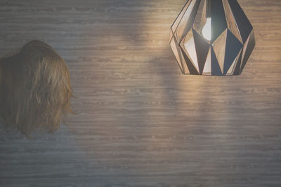 Woman and illuminated pendant light against by wall at home