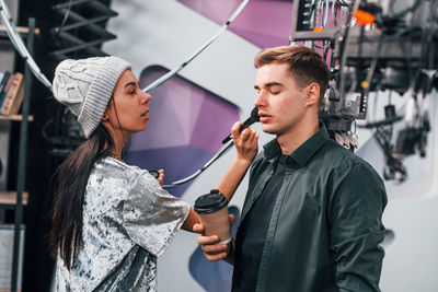 Young man is preparing for tv online broadcast. woman helps with make up.