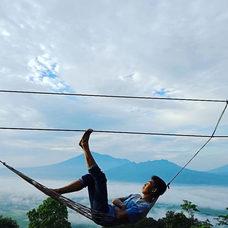 cloud - sky, real people, sky, one person, leisure activity, lifestyles, full length, casual clothing, day, nature, low angle view, blue, young women, young adult, cable, sitting, holding, connection, outdoors