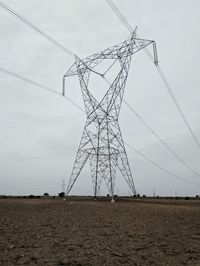 Low angle view of electricity pylon on field against sky