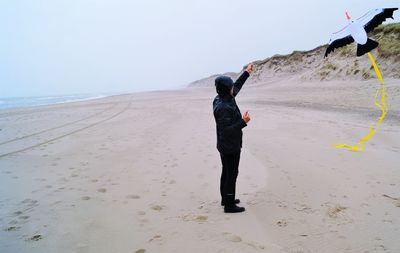 Side view of man flying kite while standing at beach