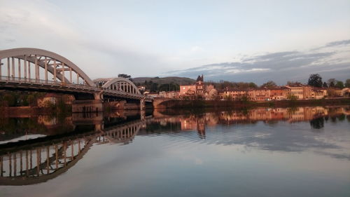 Bridge over river by buildings against sky in city