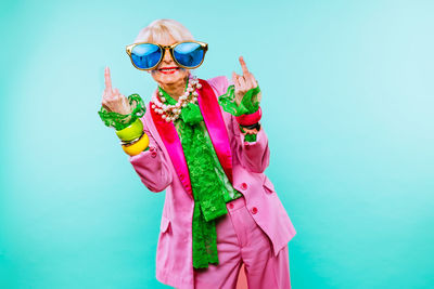 Portrait of senior woman wearing sunglasses gesturing against blue background