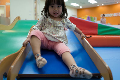 Full length of girl sitting on slide at playground