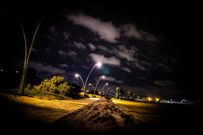 Illuminated road against dramatic sky at night