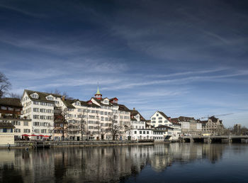 Buildings by river against blue sky