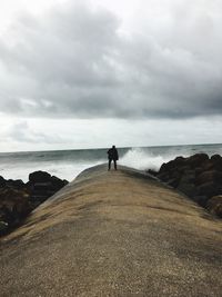 Man standing on pier by sea against cloudy sky