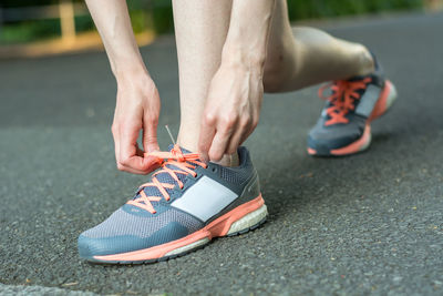 Low section of woman tying shoelace on road