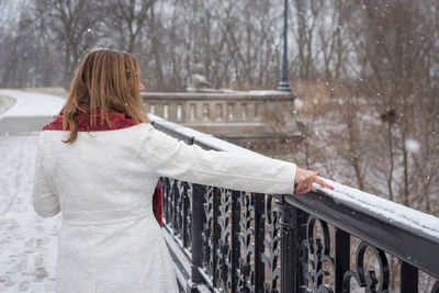 Rear view of woman touching snow on railing