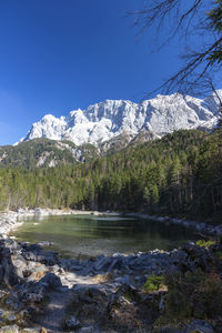 Scenic view of lake by snowcapped mountains against blue sky