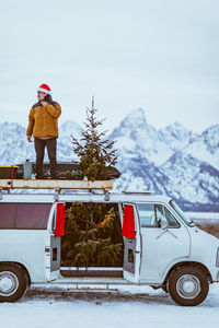 Man stands on top of white passenger van decorated for christmas christmas tree
