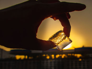 Close-up of hand holding ice against sun during sunset