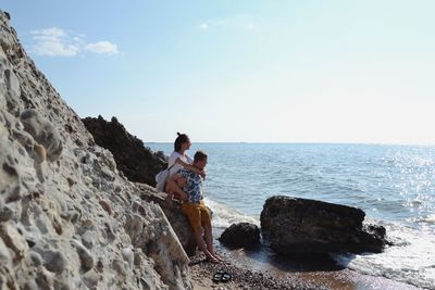 Man standing on rock by sea against sky