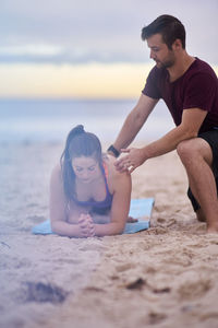 Fitness instructor assisting woman in exercising at beach