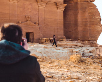 Rear view of man photographing girl walking against ancient building