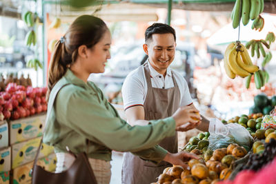 Portrait of woman holding fruits for sale at market stall