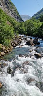 Scenic view of river flowing by mountain against sky