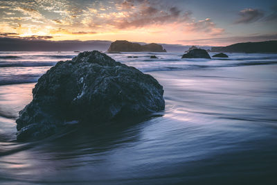 Rock formation in sea against sky during sunset