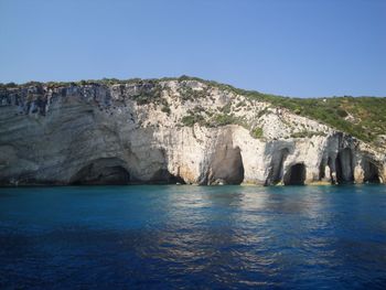 Scenic view of rock formation in sea against clear blue sky