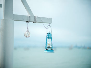 Close-up of lighting equipment hanging by sea against sky