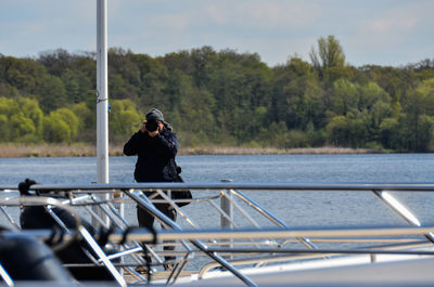 Man photographing while standing on pier against lake