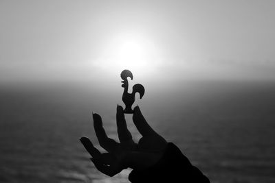 Cropped image of hand holding toy bird by sea against sky