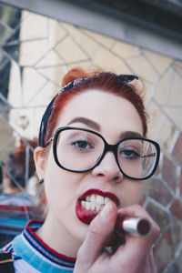 Portrait of redhead young woman applying red lipstick against mosaic wall