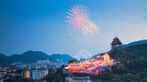 Firework display in city against sky at dusk