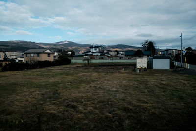 Houses on field by buildings against sky