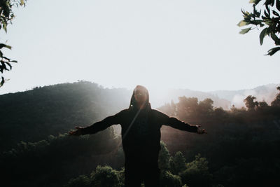 Man with arms outstretched standing on mountain against sky