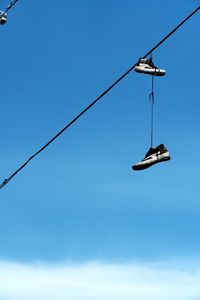 Low angle view of shoes hanging on cable against clear blue sky