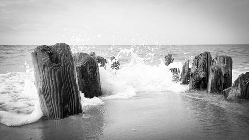 Sea waves splashing on rocks at shore against sky