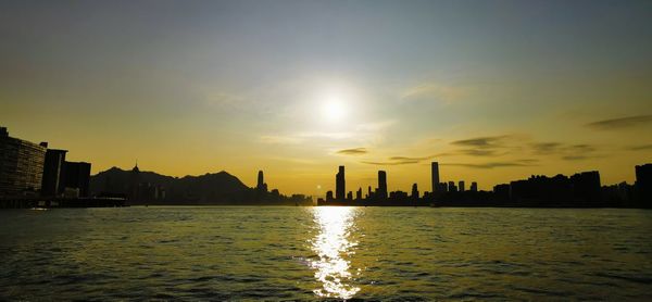 Silhouette buildings by city against sky during sunset