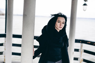 Portrait of beautiful young woman standing in gazebo against sea